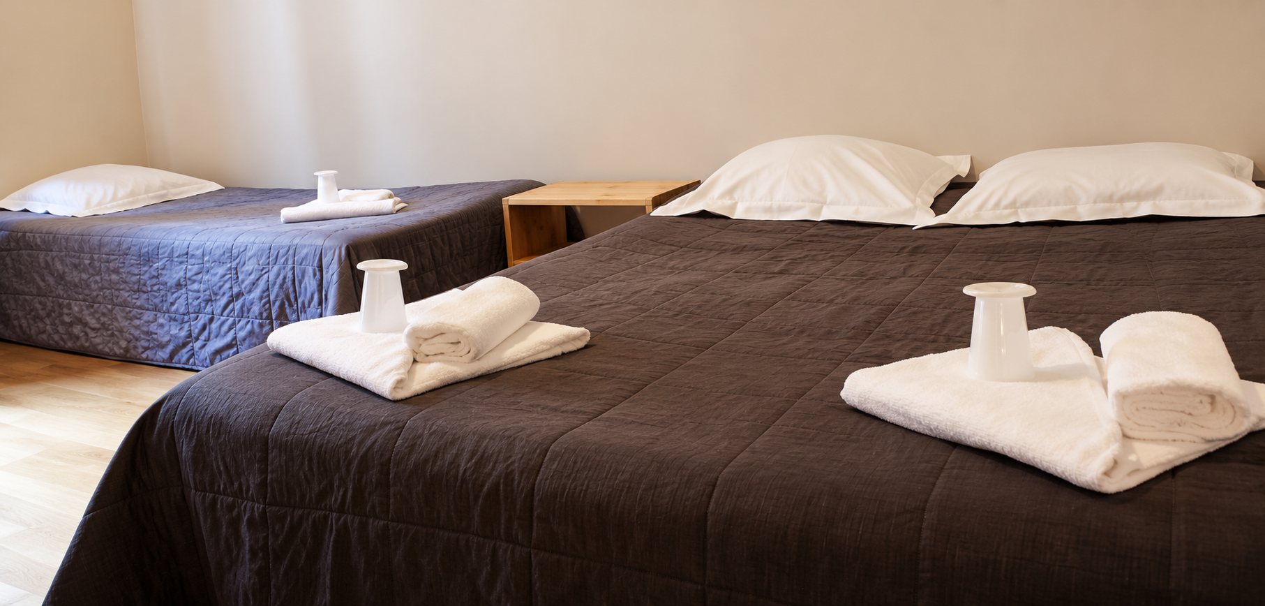 Chambre claire avec deux lits recouverts de plaids bruns, sur lesquels sont posées des serviettes blanches pliées.