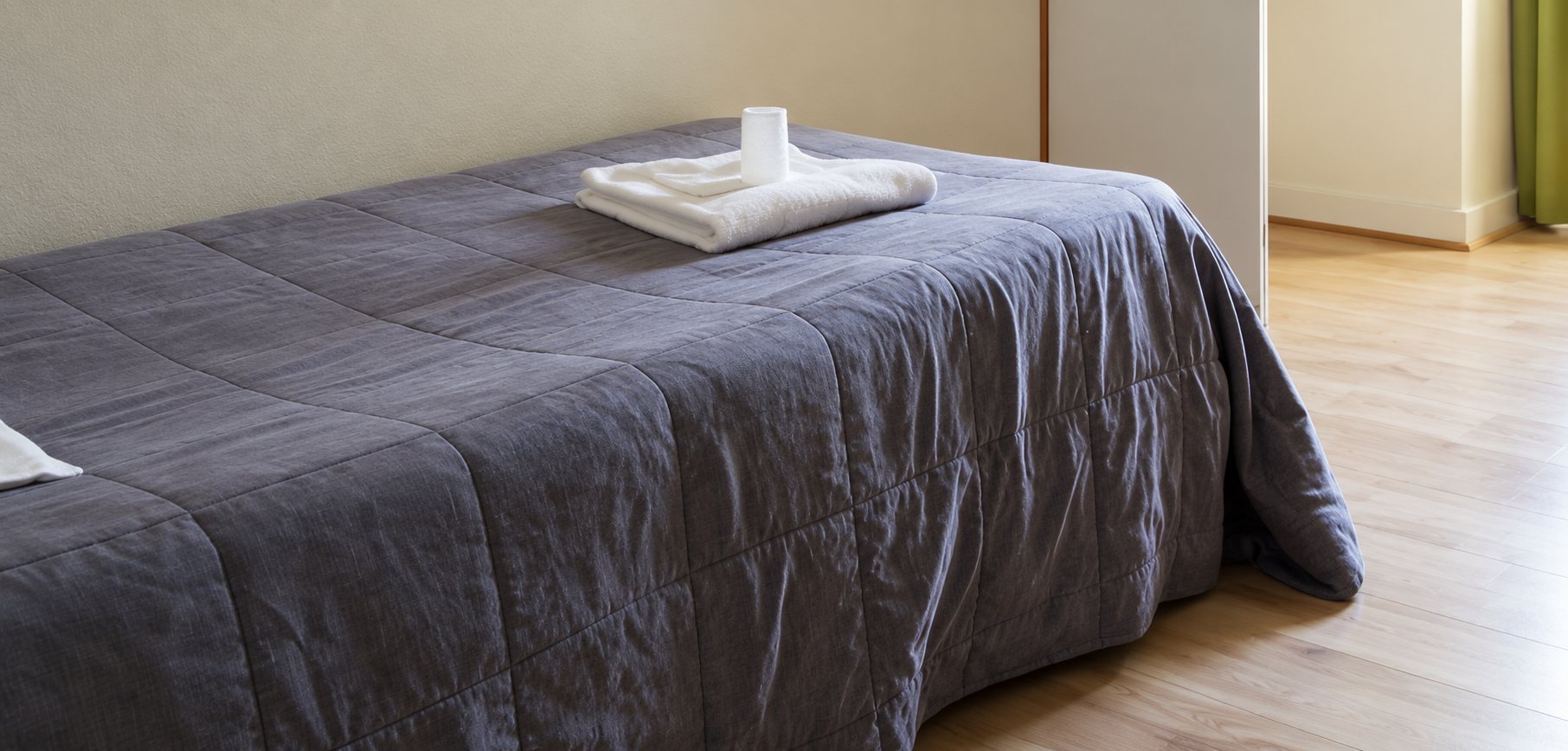 Un lit recouvert d'un couvre-lit gris avec des serviettes pliées posées dessus, sur un parquet clair.
